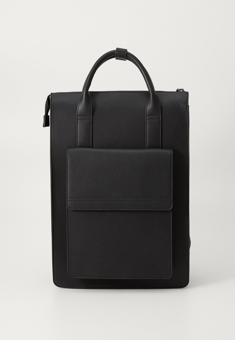 Mochila de cuero negra con un diseño minimalista. Cuenta con un asa en la parte superior, correas ajustables y un bolsillo frontal con cierre de solapa. Textura suave.