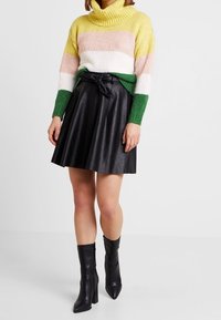 Wielokolorowy dzianinowy sweter z golfem w zielone, różowe i żółte paski, zestawiony z czarną spódnicą w kształcie dzwonu z ekologicznej skóry oraz czarnymi botkami za kostkę.