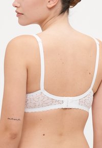 Hvit blonder bralette med justerbare stropper, bølgede kanter og en krok-og-løkke lukking bak. Myk, delikat tekstur.