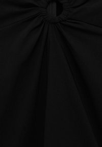 Tissu noir à texture froncée, avec une ouverture circulaire au centre et une fermeture à glissière cachée. Matériau lisse et opaque.