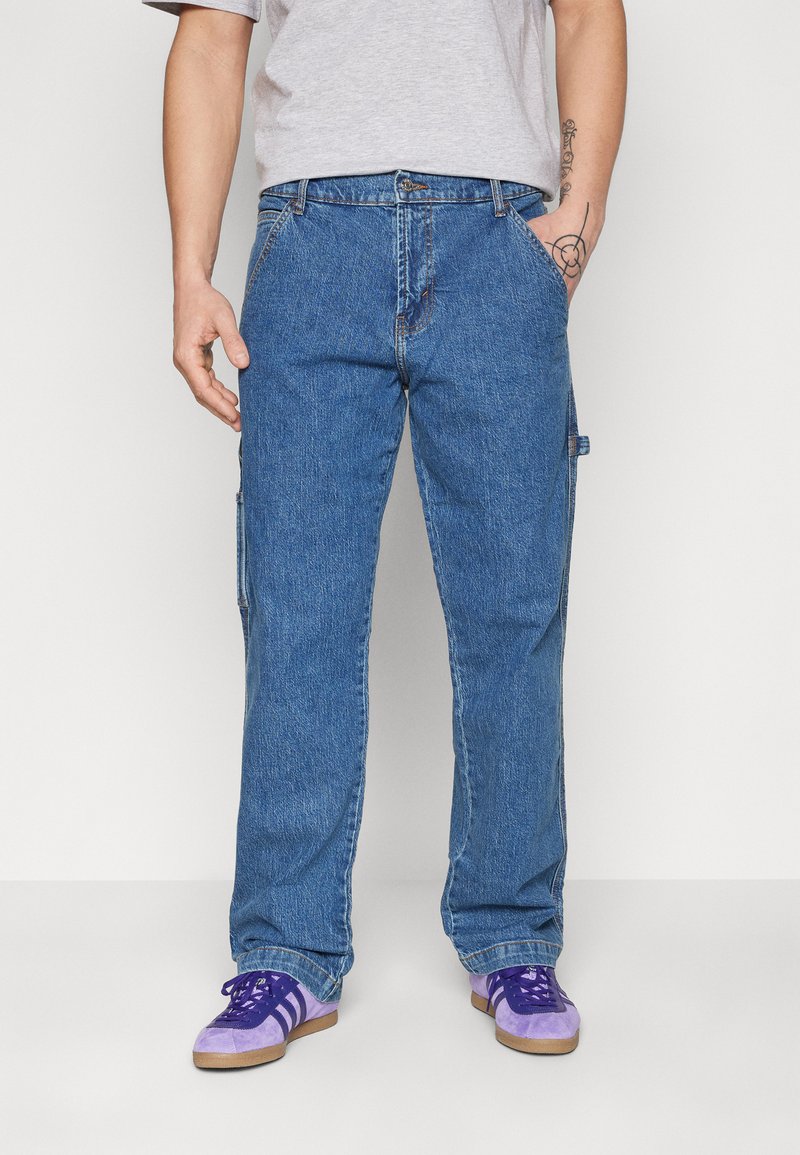 Pantaloni cargo din denim albastru cu un design drept, dotati cu buzunare laterale si un talie clasica. Purtați cu pantofi sport violeți și gri.