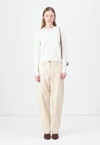 Camicia bianca a maniche lunghe e pantaloni beigi a vita alta con pieghe. Scarpe con tacco marroni. Design semplice, accenti minimalisti.
