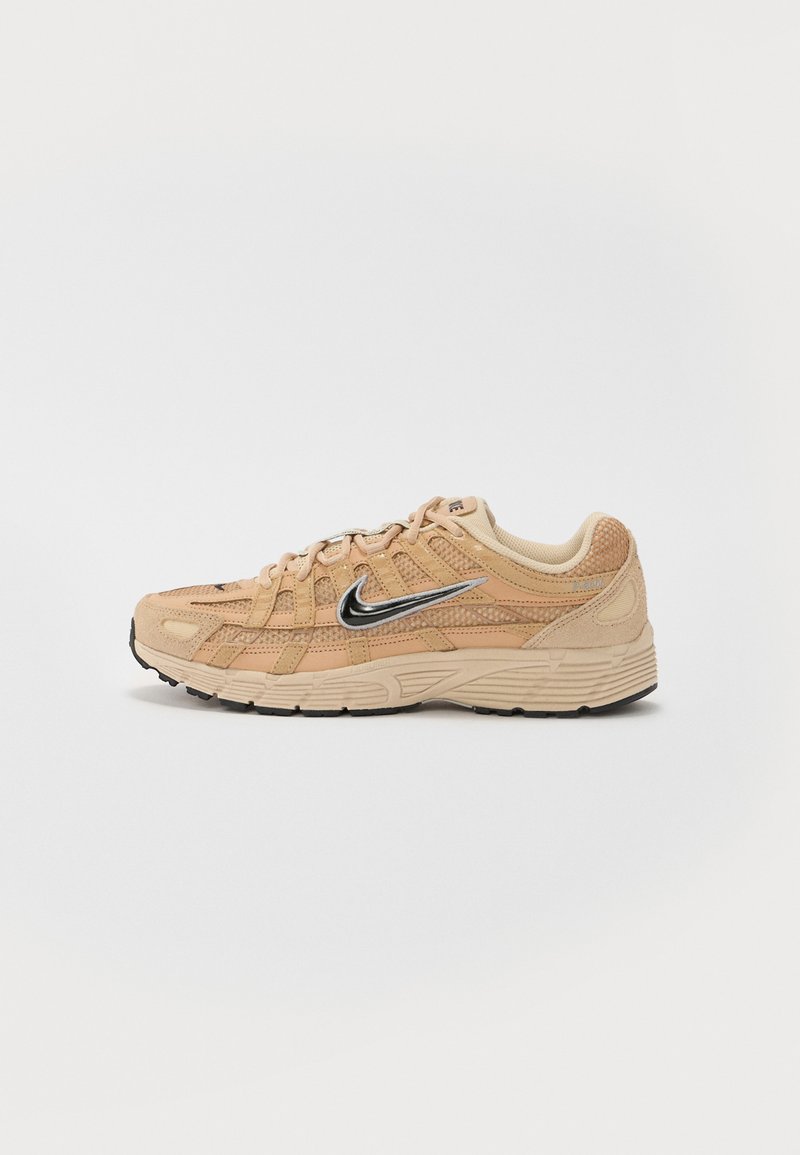 Shoe atlético bege com materiais em malha e camurça, silhueta curva, sola preta, logótipo prateado da Nike em destaque de um lado e detalhes texturizados.