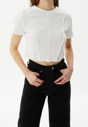 Hvid crop-top T-shirt med korte ærmer, der har lodrette sømme og en bølget bund, parret med højledede sorte jeans.