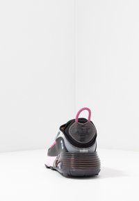 Svart och grå sneaker med rosa accenter och en texturerad sula. Har en rund bakdel med en dragflik och flerfärgade designelement.