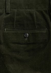 Olijf groene broek van corduroy met verticale ribbels, een achterzak met een zwarte knop en een klassiek ontwerp.