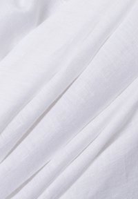 Witte linnen stof met een gestructureerd oppervlak, met subtiele natuurlijke variaties. Het materiaal is zacht en valt elegant in zachte plooien.