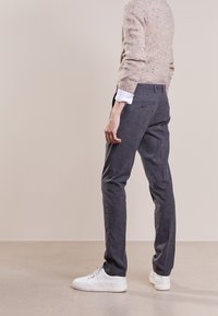 Pantaloni grigi su misura realizzati in un tessuto leggero, dotati di tasche posteriori e una vestibilità slim, abbinati a sneakers bianche e un maglione beige.
