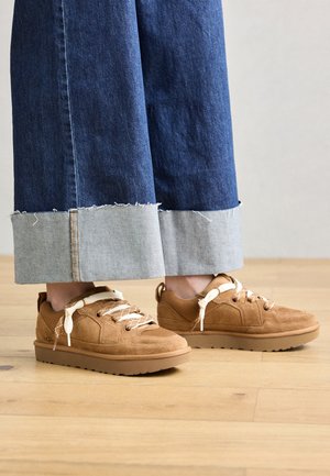 Bruine suede sneakers met textuurpanelen en lichtgekleurde veters. Gecombineerd met blauwe denim broeken met wijde pijpen en rafelige zoom.