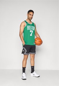 Grøn basketballtrøje med hvid tekst "BOSTON" og nummer "7", parret med sorte shorts med hvide detaljer, hvide sneakers og en basketball.