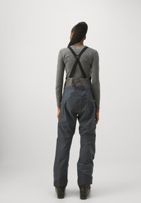 Harmaa pitkähihainen paita yhdistettynä tummiin vesitiiviisiin haalarikappaleisiin, joissa on säädettävät olkaimet ja sivutaskut. Sujuva, toimintakykyinen kangas.