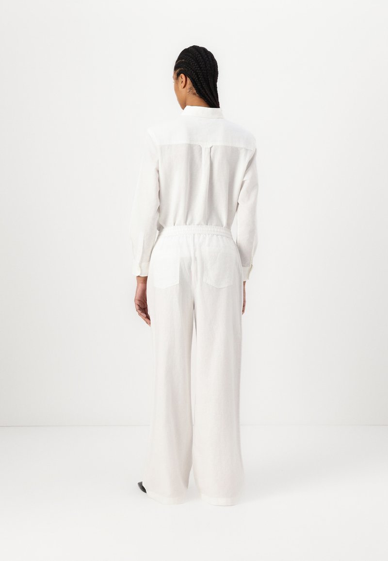 Witte linnen twee-delige outfit met een langarm overhemd met een knoopsluiting aan de achterkant en wijdvallende broek met een elastische tailleband en achterzakken.