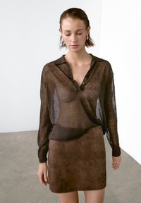 Brun semi-gennemsigtig langærmet skjorte med krave og knapper, parret med en brun mini nederdel, hvilket skaber en lagdelt tekstureffekt.