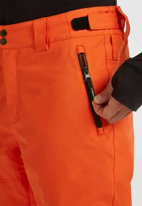 Heldere oranje skibroek heeft een functionele zijrits-zak, een verstelbare taille en een duurzame stof met een gladde textuur.