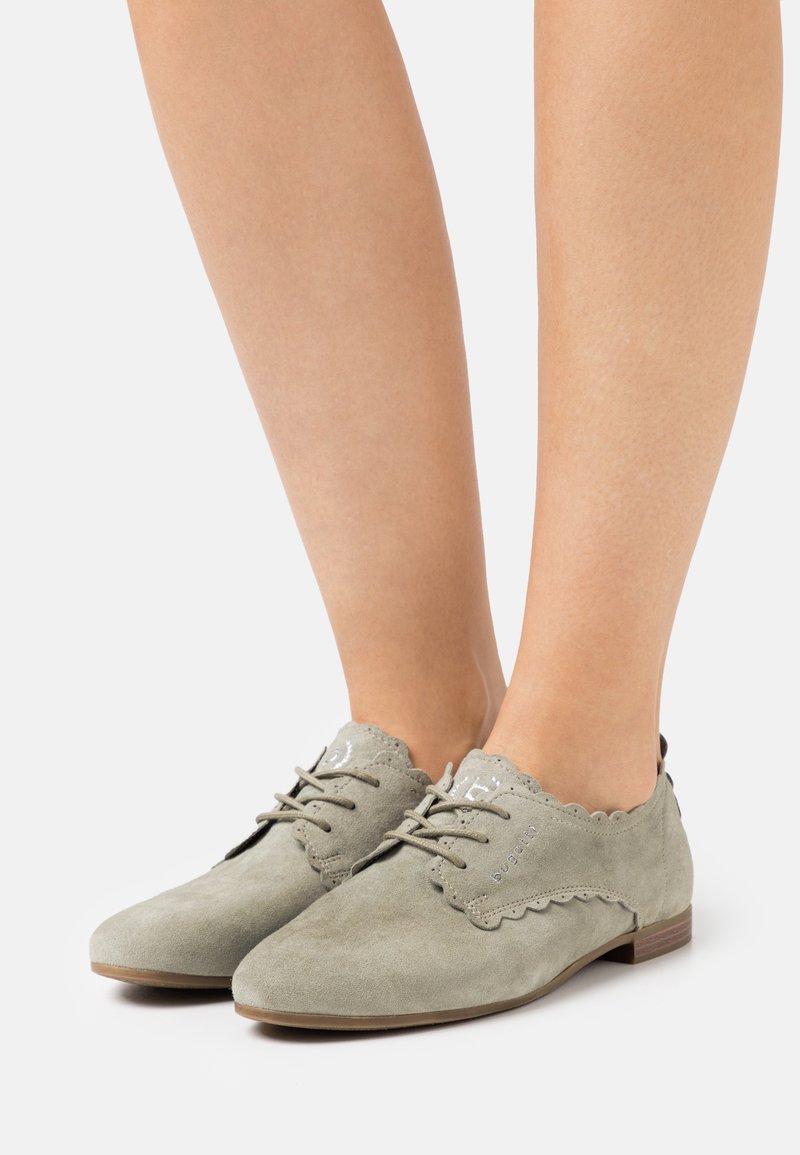Zapatos oxford de ante verde con bordes ondulados, puntera redondeada y suela de madera plana. Los cordones en la parte frontal añaden un detalle funcional.