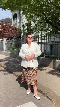 White double-breasted blazer over a leopard print slip skirt, white pointed flats, and round sunglasses, with a small white handbag.