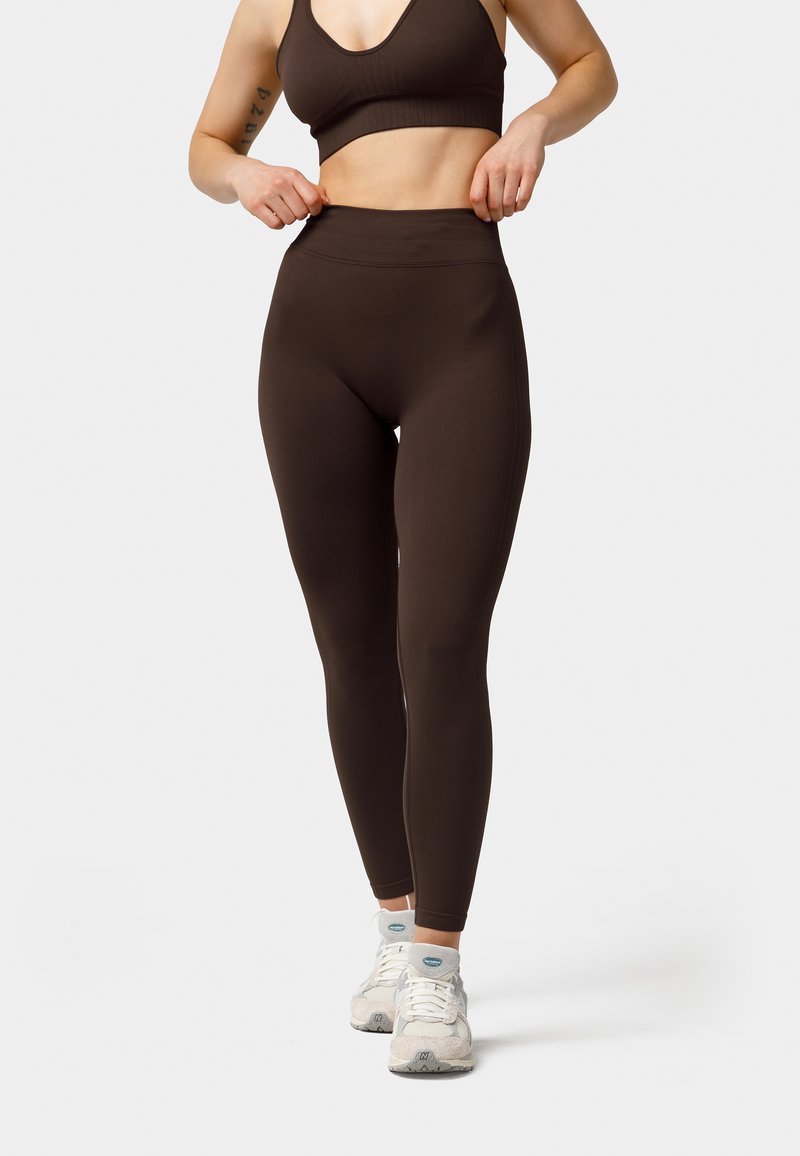 Braune Sportleggings, hochgeschnitten mit einer glatten Textur. Kombiniert mit einem passenden Crop-Top und hellen Sneakers mit Akzenten.