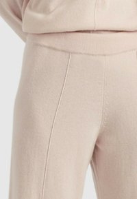 Pantaloni a maglia rosa chiaro con una texture morbida, dotati di una vita a coste e dettagli di cucitura verticale lungo le gambe.