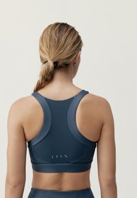 Námořnická sportovní podprsenka s elegantním designem, vyrobená z hladkého, elastického materiálu. Má široké ramínka a minimalistické logo na zadní straně.