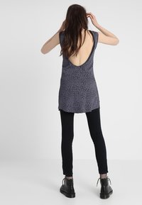 Short-sleeve top with a deep V-back, featuring a dark gray leopard print design, paired with black leggings and black ankle boots.