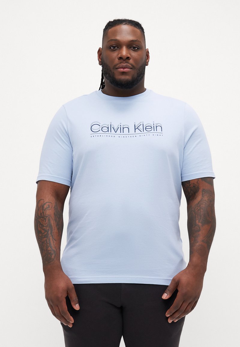 Svijetloplavi majica kratkih rukava s logom "Calvin Klein" u nešto tamnijoj plavoj boji. Pamučni materijal; glatka tekstura; okrugli izrez.