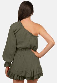 Robe asymétrique vert olive avec une longue manche bouffante, un ourlet volanté et un tissu texturé. Taille élastique pour un ajustement silhouette.