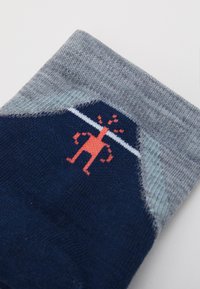 Marineblau- und graue Socken mit einem Design von einem korallenroten Cartoon-Figur, mit einem kurzen grauen Bündchen und weißen Streifendetails. Weiches Strickmaterial.