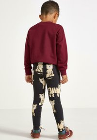 Bordeauxtröja och svarta leggings med gul tigerprint. Tröjan har rund halsringning; leggings har en elastisk midja.