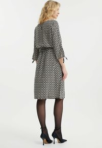 Abito a righe bianco e nero con maniche a tre quarti, vita sagomata e gonna al ginocchio. Indossato con tacchi alti neri e collant velati.