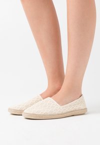 Bílé pletené plátěné slip-on boty s texturovaným povrchem a světle béžovou podešví, s kulatou špičkou a bočním elastickým páskem pro snadné obouvání.