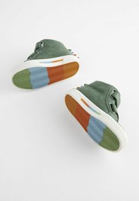 Zelené plátěné vysoké boty s bílými podrážkami, které mají barevné gumové dno se vzorem zigzag v modré, zelené, oranžové a žluté barvě.