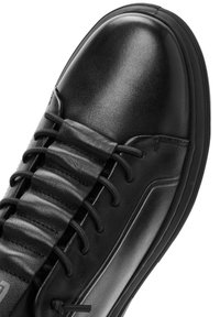 Zwarte leren sneakers met een gladde textuur, voorzien van platte veters en een rubberen zool. Het design omvat gebogen stiksels en een slanke silhouet.