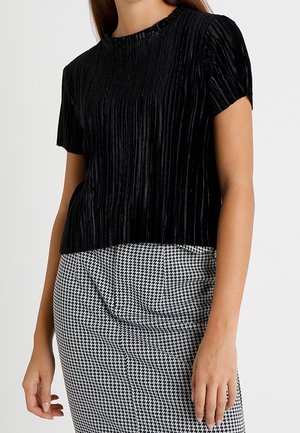 Czarny krótki top z pionowymi plisami, wykonany z teksturowanej tkaniny. Połączony z wysokim stanem spódnicy w kratę psyhgodną.