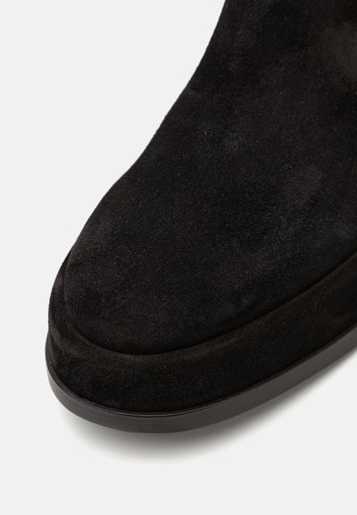 Cizmă ankle din daim negru cu vârf rotund și talpă plată din cauciuc, având o textură netedă și un design minimalist.