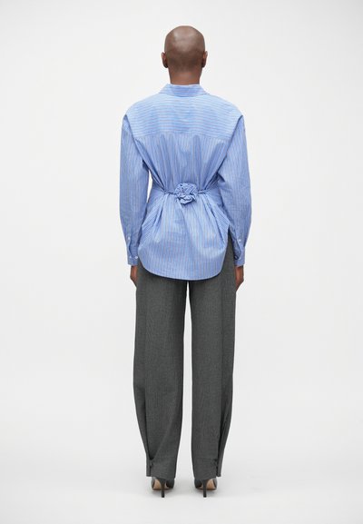 Blauw-wit gestreepte oversized blouse met een geplooide achterkant, gecombineerd met hoog-wijde grijze broeken met een gestructureerd patroon.