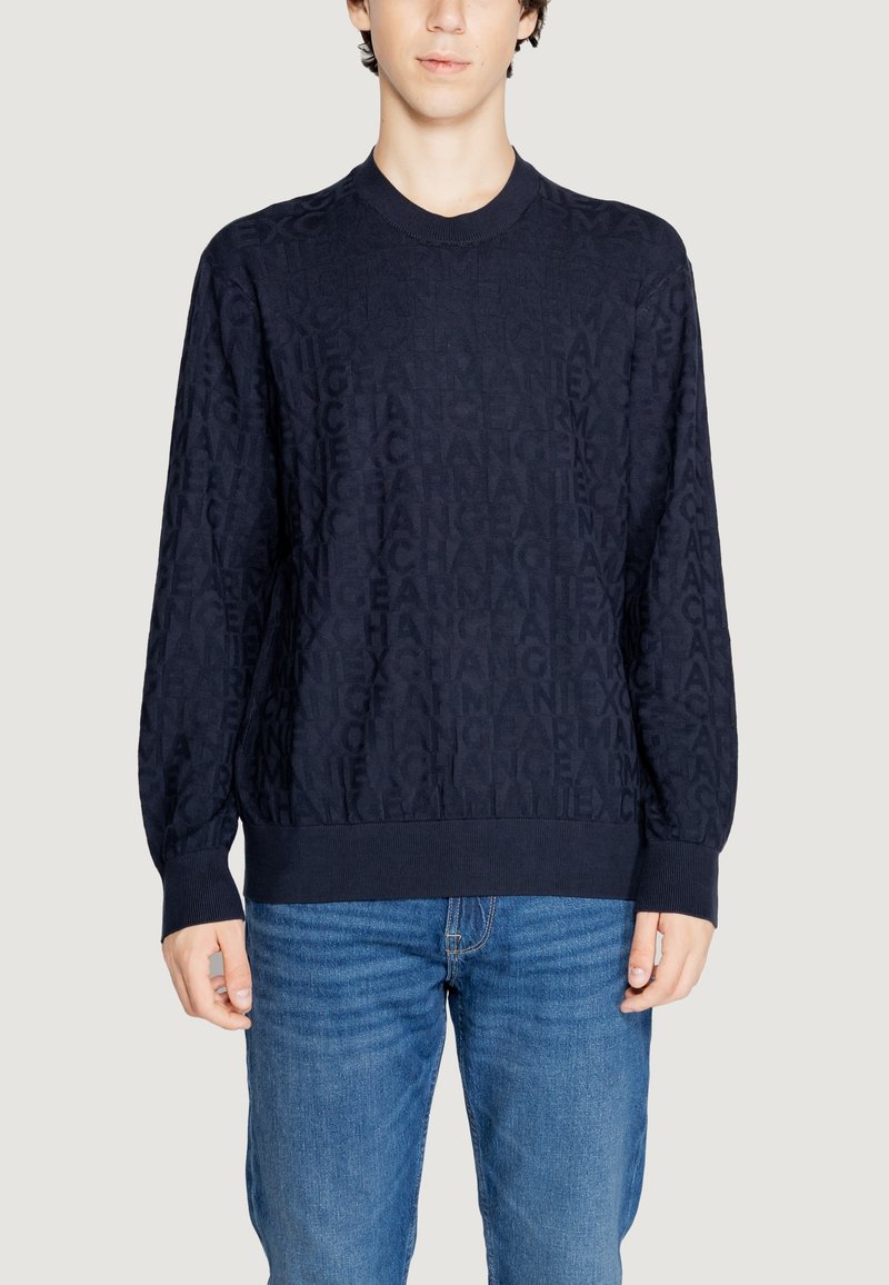 Maglione blu navy caratterizzato da un motivo testurizzato di lettere ripetute, scollo rotondo e polsini e vita a costine. Abbinato a jeans blu.