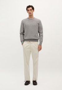 Grijze gebreide trui met ronde hals, crèmekleurige broek en donkerbruine schoenen. Eenvoudig ontwerp, nauwsluitende vorm, minimale details.