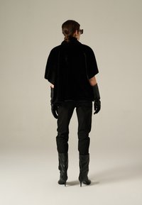 Black faux fur cape with short sleeves, paired with fitted black trousers and shiny black knee-high stiletto boots. Black leather gloves included.