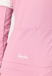 Różowa koszulka rowerowa z gładkiego materiału, z przednią kieszonką i białym logo Rapha. Projekt zawiera kontrastujący kolor rękawów.