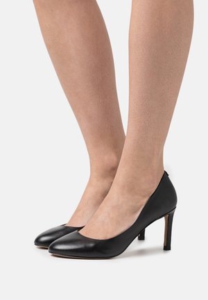 Chaussures à talons hauts en cuir noir avec un bout rond et un design épuré, présentant une texture lisse et un talon fin.