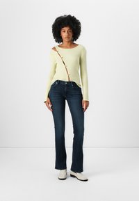 Lys grønn, ribbestrikket langermet topp med knappedetalj på siden, sammen med mørkeblå slengjeans og hvite ankelstøvler. Enkelt design.