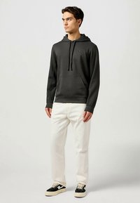 Sötétszürke kapucnis pulóver elülső zsebbel, fehér nadrággal és krémszínű talpú fekete tornacipőkkel párosítva. Egyszerű, hétköznapi kialakítás.