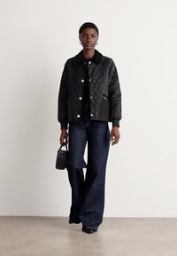 Black quilted jacket with round gold buttons, paired with dark denim flared pants. Accessorized with a small black handbag.