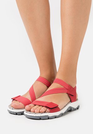 Sandales rouges avec des sangles tressées, comprenant une semelle intérieure texturée et une semelle blanche flexible avec des accents gris. Conception à bout ouvert.