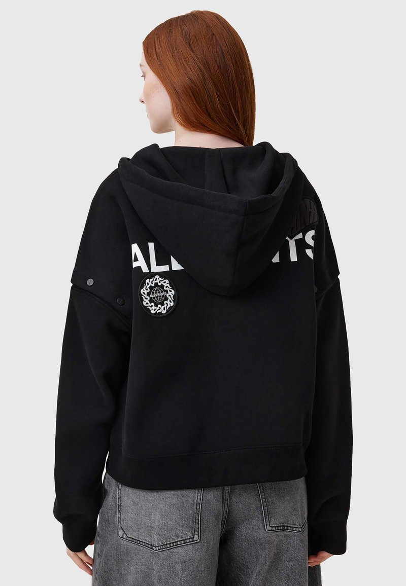 Sudadera negra con capucha de corte holgado, que presenta el texto gris "ALL" y un parche circular en la parte de atrás. La tela tiene una textura suave y lisa.