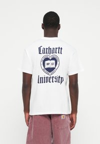 White cotton t-shirt featuring a large navy blue graphic on the back with "Carhartt University" and additional text in a bold font.