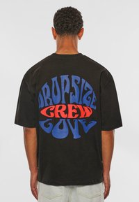 Sort T-shirt med stort grafisk teksttryk på ryggen i rød og blå. Løs pasform med korte ærmer og rund halsudskæring.