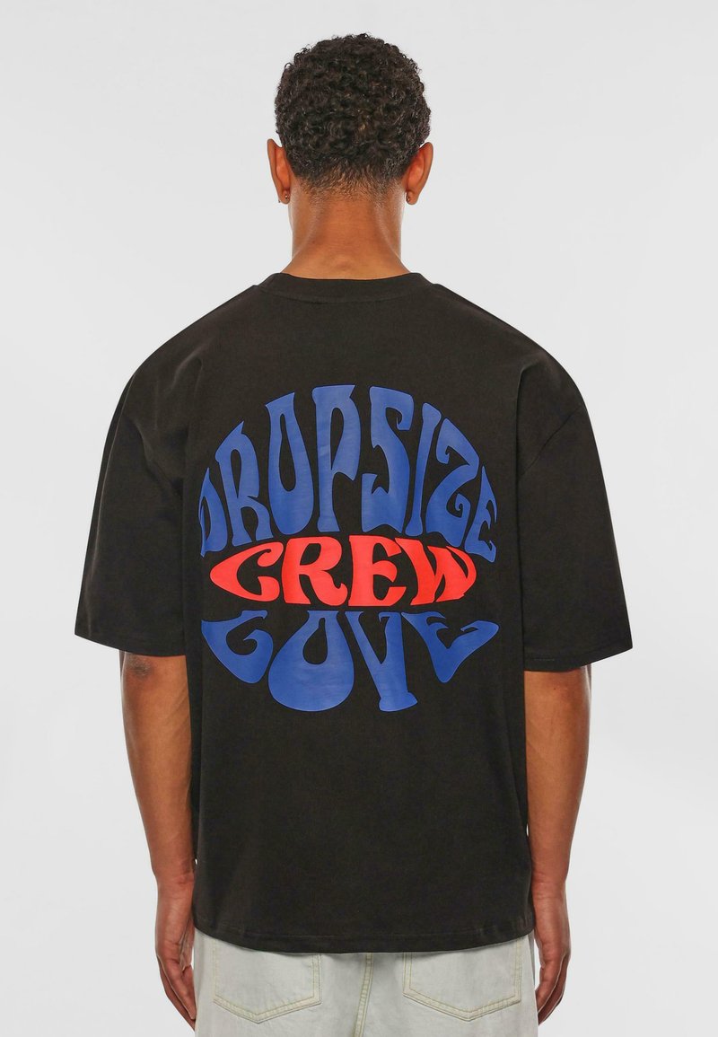 Sort T-shirt med stort grafisk teksttryk på ryggen i rød og blå. Løs pasform med korte ærmer og rund halsudskæring.