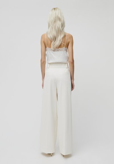 Weißes Satin-Camisole mit Spitzenbesatz, kombiniert mit hoch-taillierten, weiten Hosen. Glatter Stoff mit fließender Silhouette.