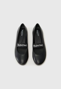 Sapatos pretos planos com um acabamento em couro liso, bico arredondado e uma tira com a palavra "VALENTINO" em branco. Design simples e elegante.